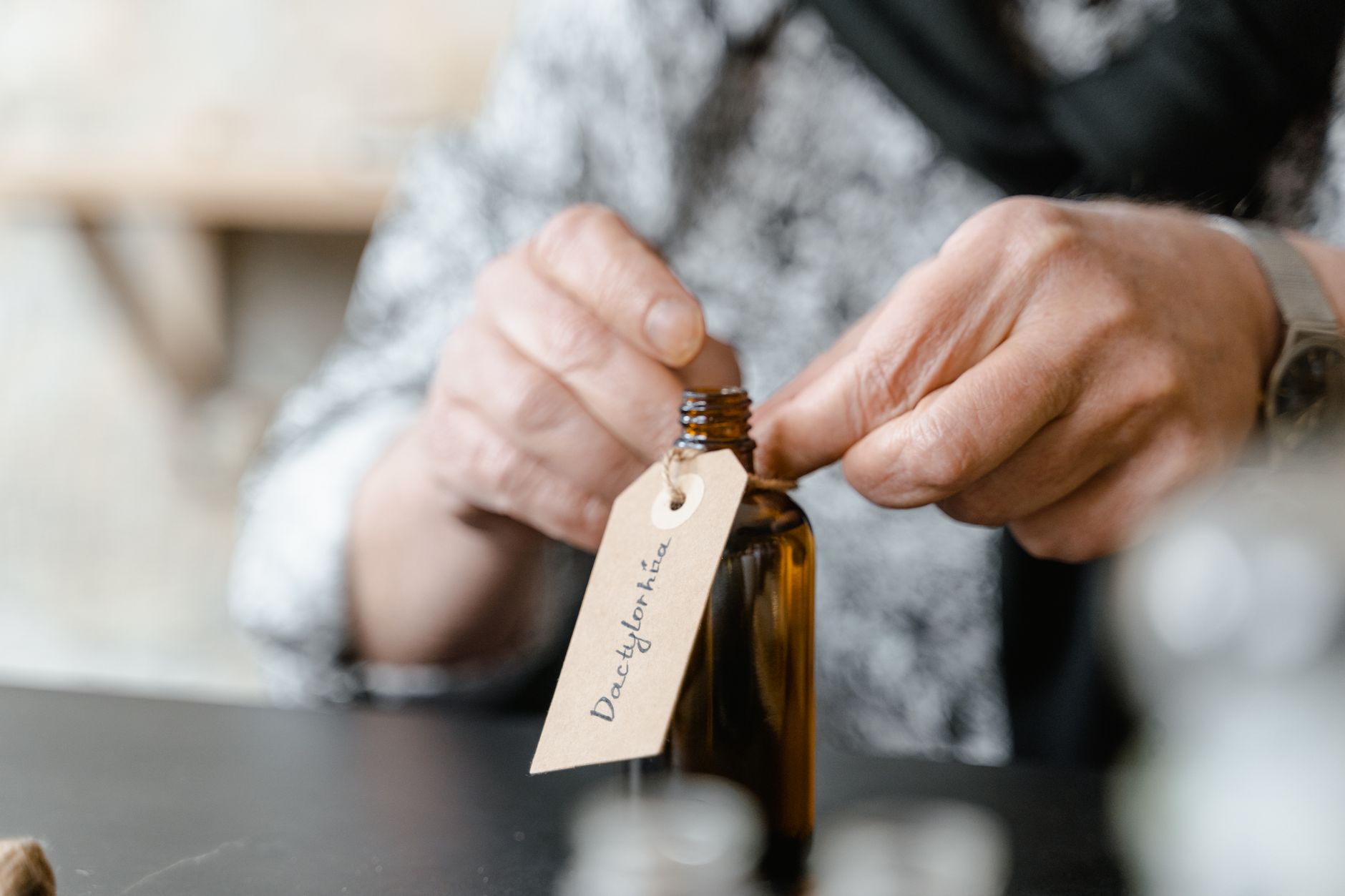 Close-up of a person attaching a label to a brown glass bottle indoors.