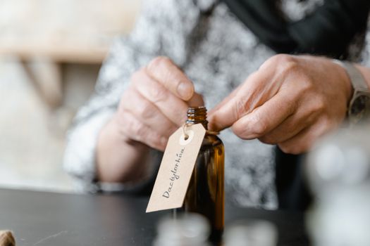 Close-up of a person attaching a label to a brown glass bottle indoors.