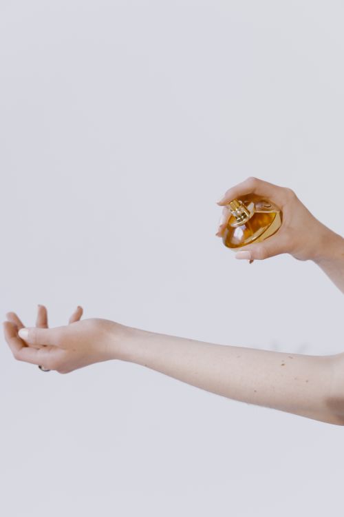 Free Close-up of a hand spraying perfume on a wrist against a soft white background. Stock Photo