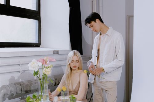 Free A man and woman interact in a sunlit room with a floral arrangement on the table. Stock Photo