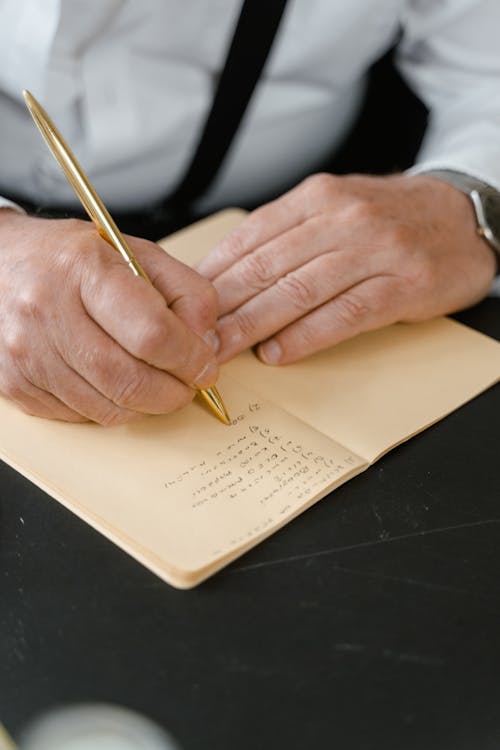 Person Holding a Gold Pen Writing on Notebook