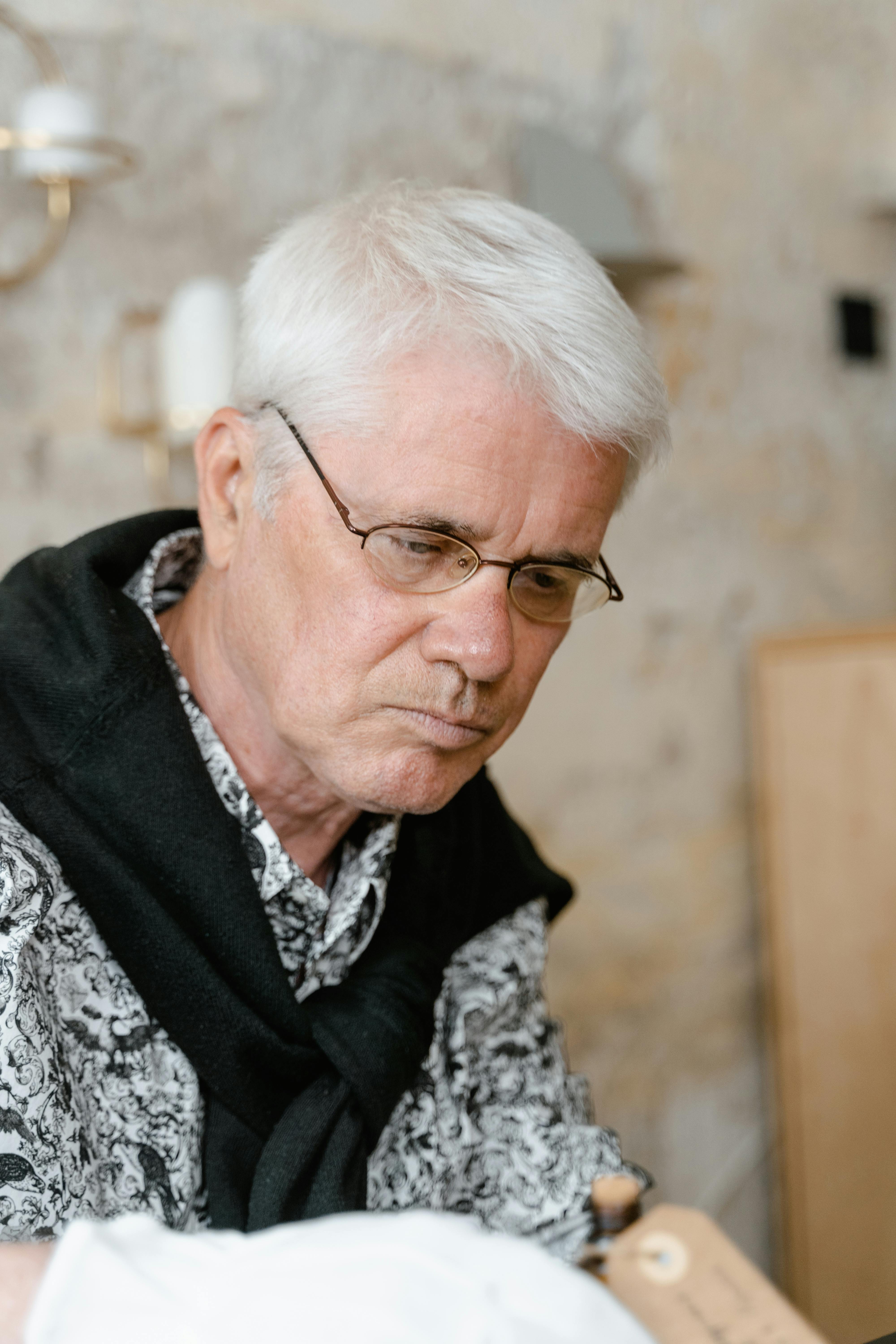 Senior man with white hair and glasses indoors looking thoughtful.