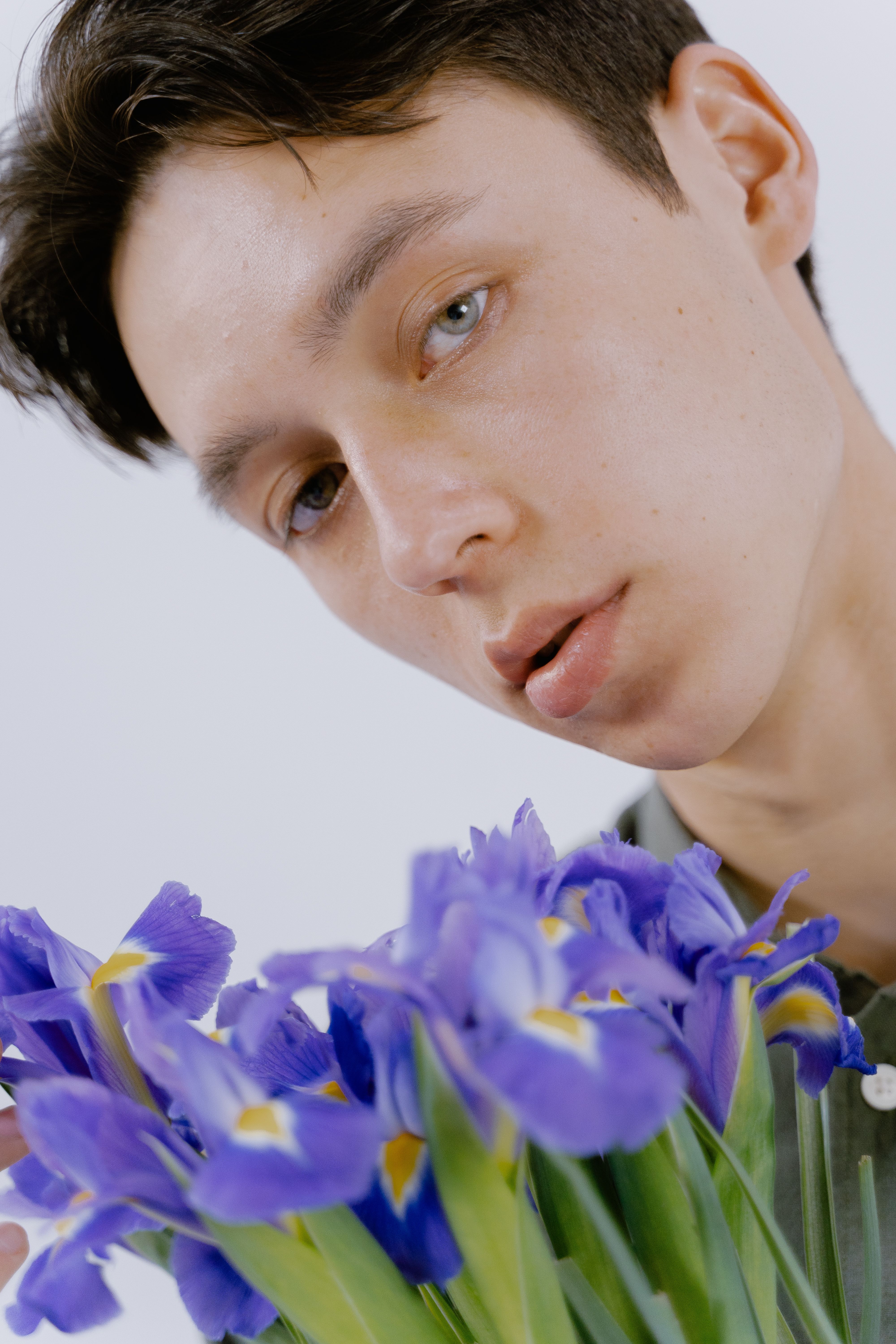 A young man in a close-up shot holding a bouquet of vibrant purple flowers against a white background.