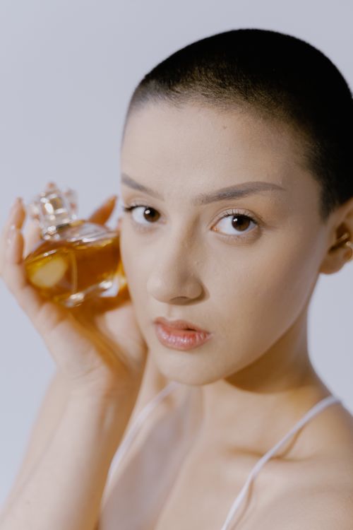 Free Close-up portrait of a bald woman holding a perfume bottle. Stock Photo