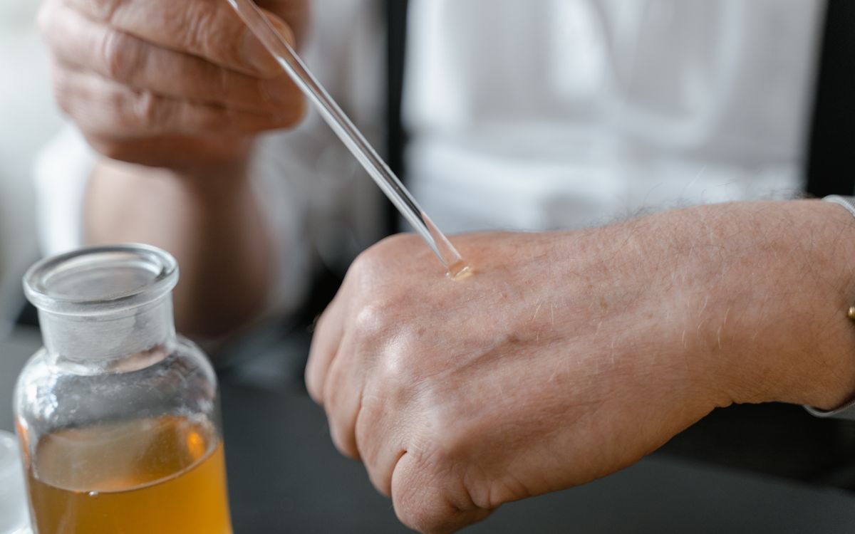 Close-up of a person applying perfume on their hand with a dropper, showcasing the art of fragrance testing.