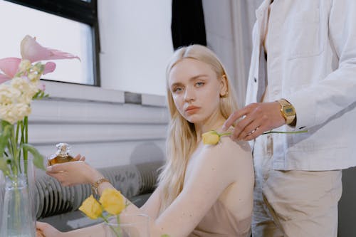 A Woman Sitting Holding a Perfume Beside Person Wearing White Denim Jacket