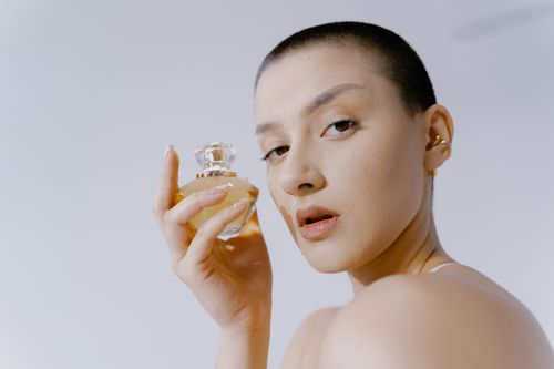 Free Close-up portrait of a woman with short hair holding a perfume bottle, showcasing elegance and style. Stock Photo