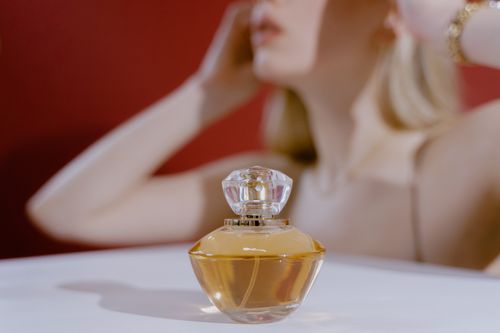 Free Stylish perfume bottle with a blurred woman in the background, capturing elegance and aroma. Stock Photo