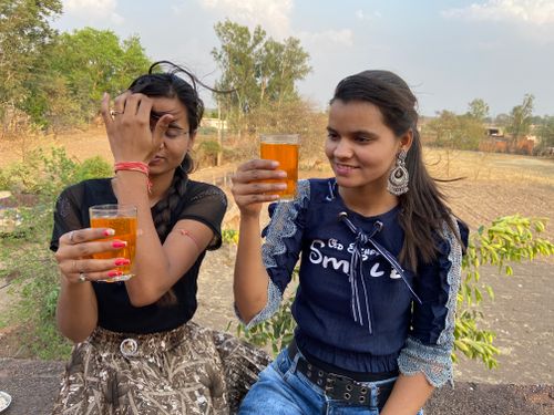 Free Two young South Asian women holding glasses with orange liquid, enjoying a moment outdoors. Stock Photo