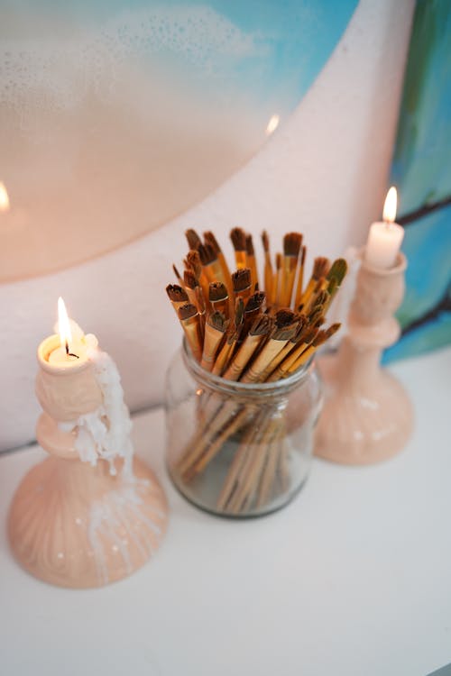 Free Assorted  Make-up Brushes in a Clear Glass Jar between Candlelights Stock Photo