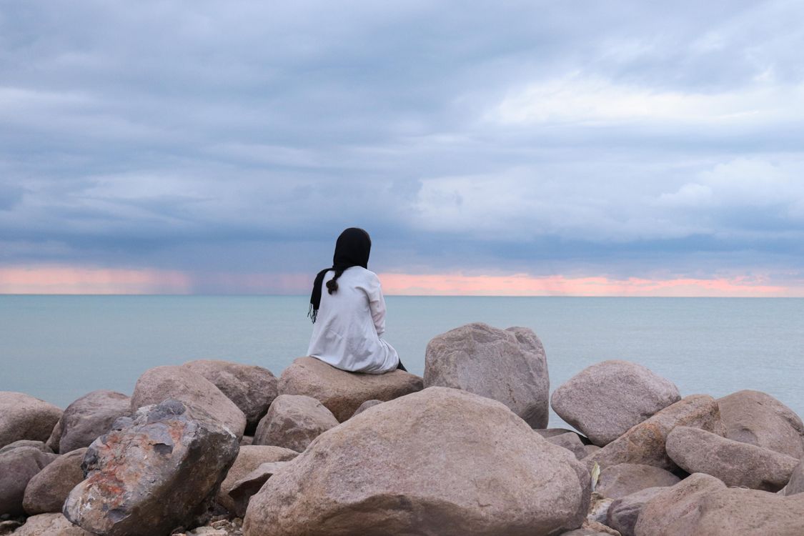 Woman in White Dress Sitting on Boulderrs on Seaside · Free Stock Photo