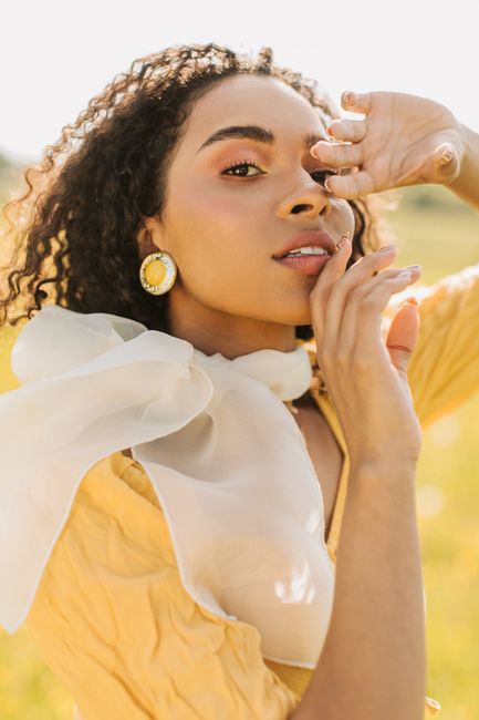 Stylish woman with curly hair posing outdoors in sunlight with a fashionable scarf accent.