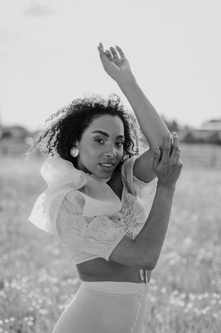 Elegant black and white portrait of a woman posing in a field, showcasing fashion and natural beauty.