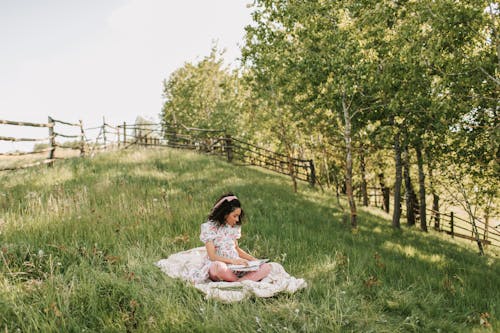 Free A Woman Wearing Dress Sitting on the Grass While Reading a Book Stock Photo