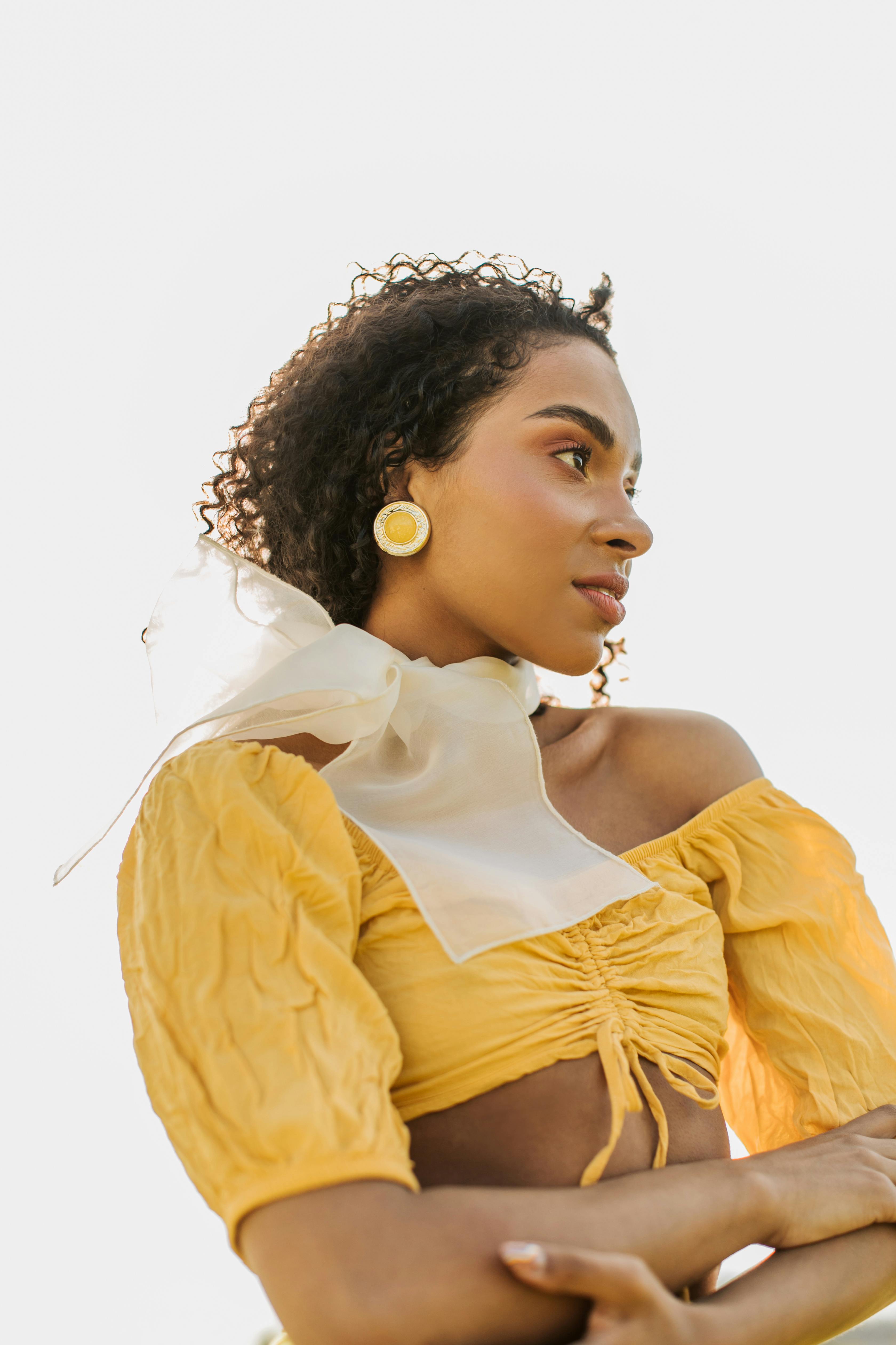 Elegant portrait of a woman in a yellow crop top with curly hair and a scarf, posing stylishly.