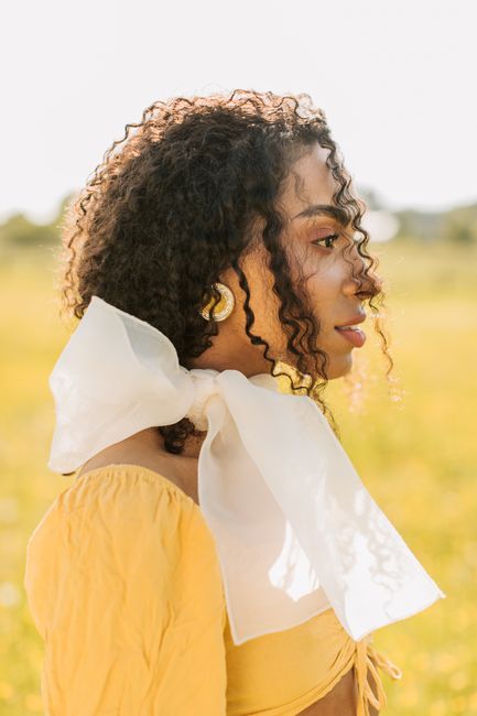 Stylish woman with curly hair and scarf photographed outdoors in natural light.