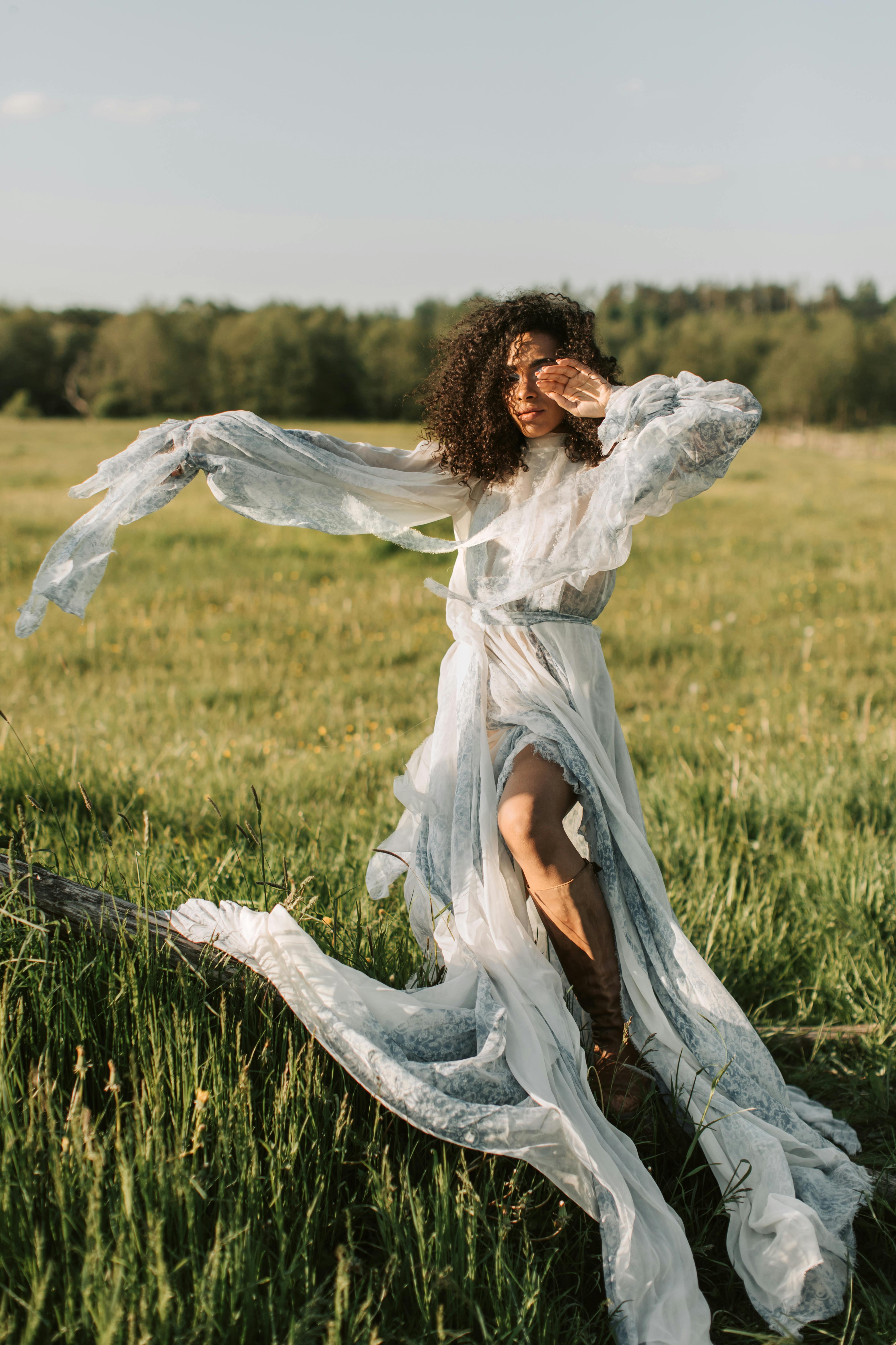 A woman in a flowing dress poses gracefully in a sunlit meadow capturing elegance and fashion.