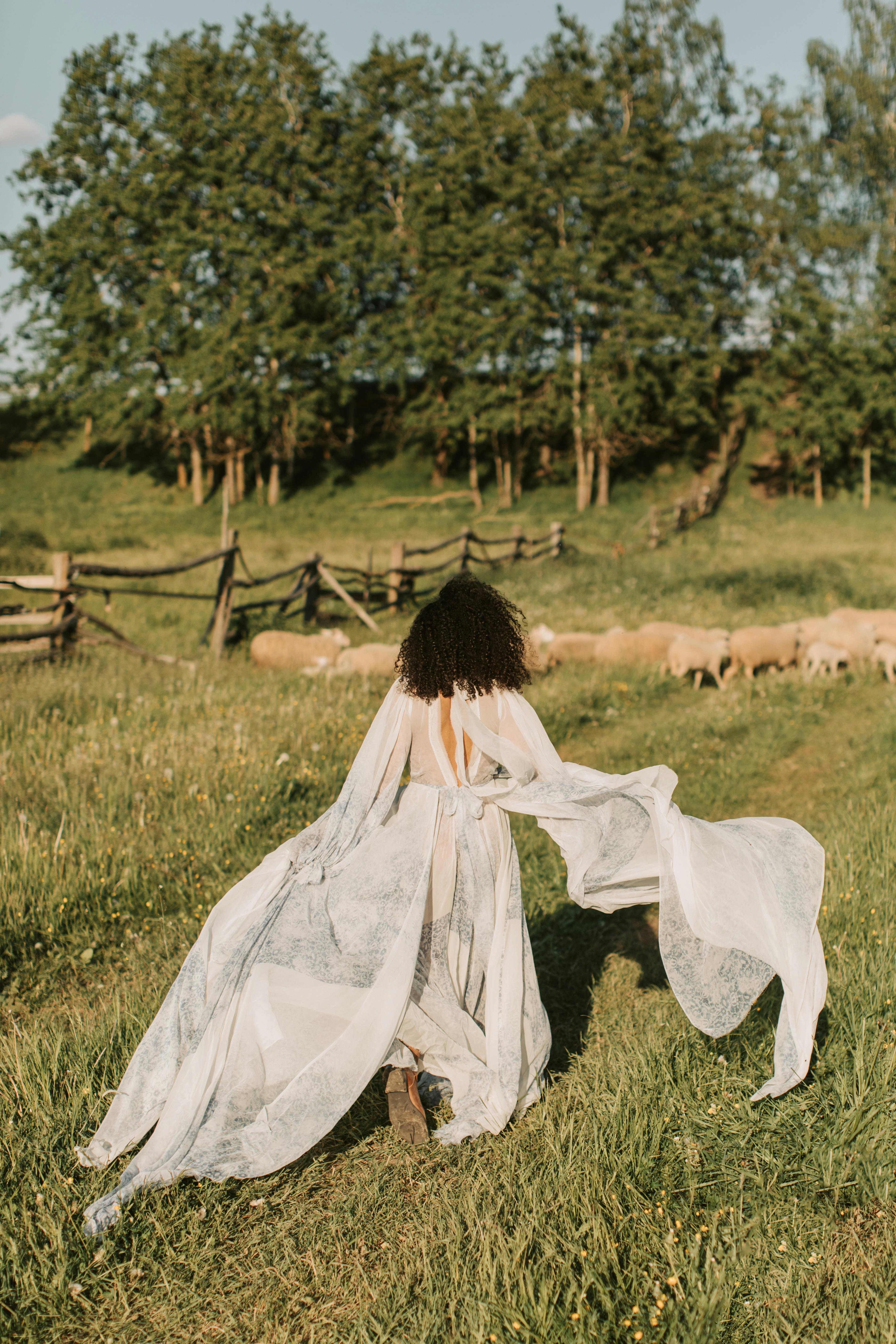 A woman in a white dress elegantly runs through a grassy outdoor setting, embracing nature.