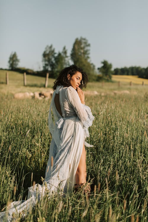 A Woman in White Dress Standing on Green Grass Field