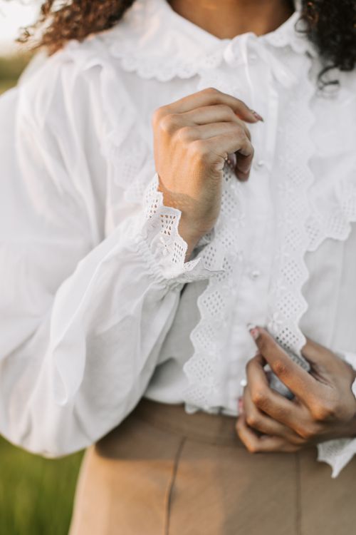 Free Detailed close-up of a woman adjusting the lace on her elegant white blouse outdoors. Stock Photo