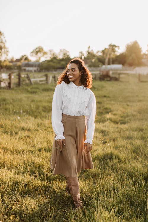 Woman in White Long Sleeve Shirt and Brown Skirt Standing on Green Grass Field