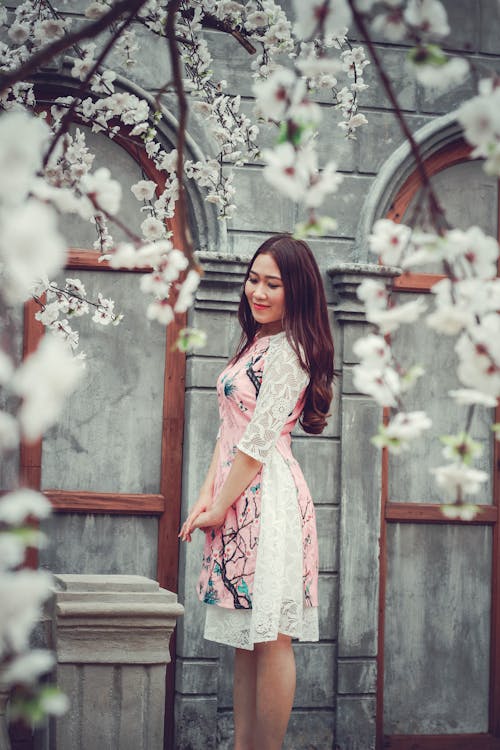 Woman Standing Beside Gray Concrete Building and Tree at Daytime