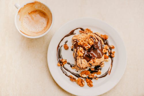 Top view of delicious homemade dessert with chocolate glaze topped with walnuts and cup of fresh cappuccino with froth