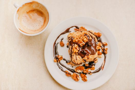 Top view of delicious homemade dessert with chocolate glaze topped with walnuts and cup of fresh cappuccino with froth