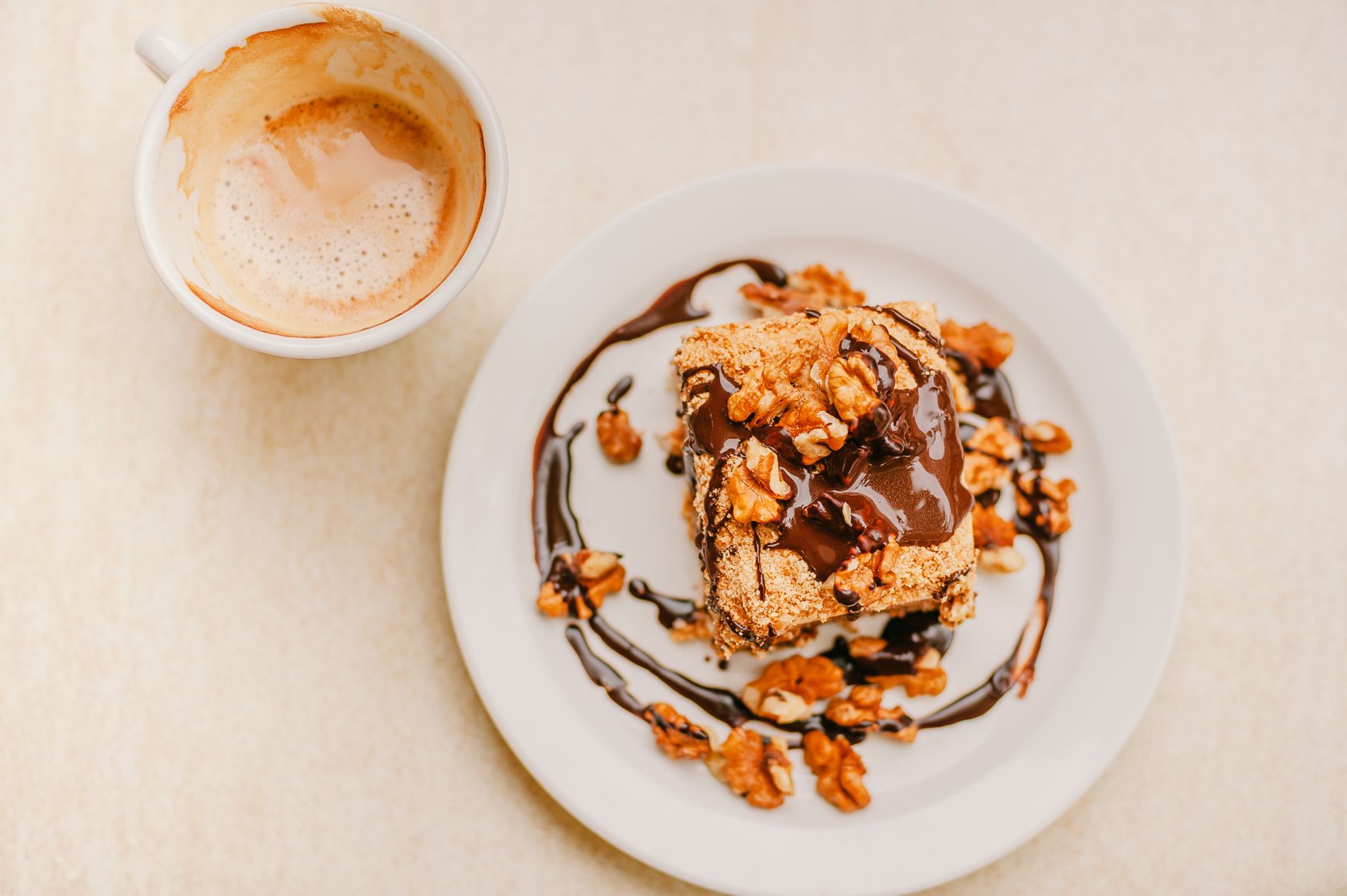 Top view of delicious homemade dessert with chocolate glaze topped with walnuts and cup of fresh cappuccino with froth