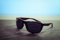 海滩边的木桌上放着一副黑色太阳镜，深色镜片提供别致的夏季保护