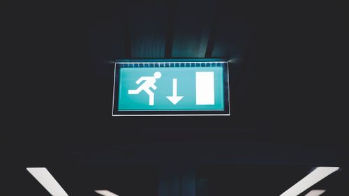 Free Brightly lit emergency exit sign with arrow indicating direction, set against a dark backdrop. Stock Photo