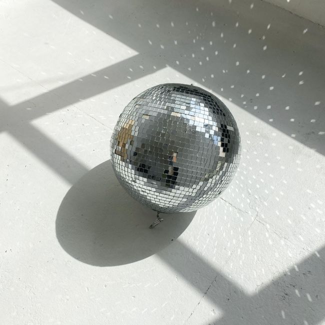 A silver disco ball casting reflections and shadows on a white surface.