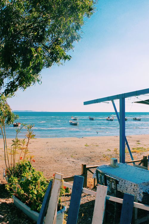 Free Peaceful beach scene with boats, trees, and a wooden patio by the ocean. Stock Photo