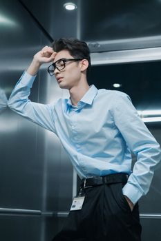 Business professional in blue shirt and glasses inside an elevator, striking a thoughtful pose.