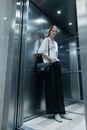 A Woman in Black Pants and White Shirt Standing Inside the Elevator