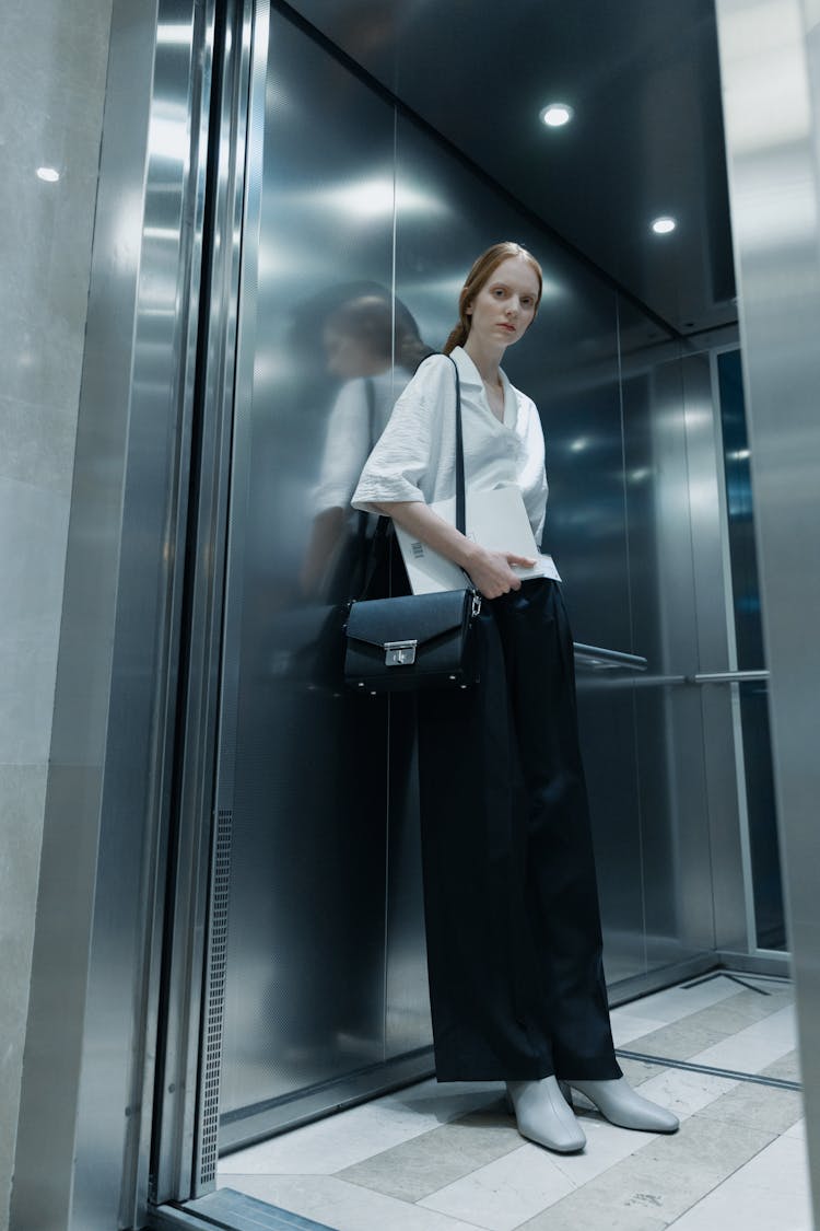 A Woman In Black Pants And White Shirt Standing Inside The Elevator