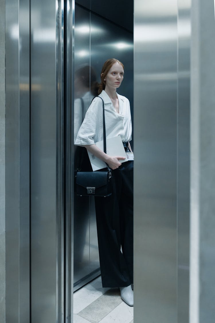 A Woman In White Button-Up Shirt Standing Inside The Elevator