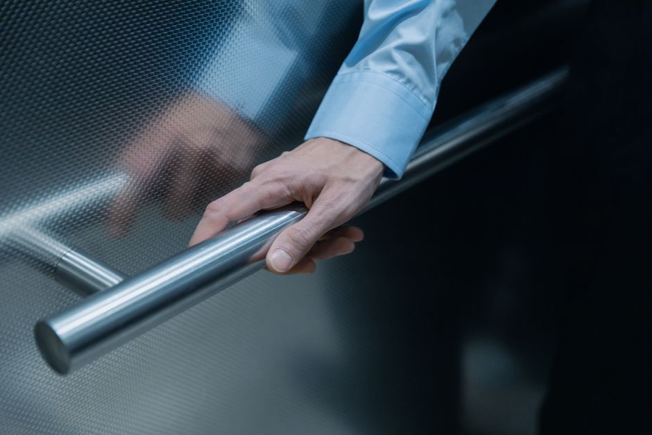 Close-up of a hand in a blue shirt holding onto a metal handrail in an elevator.
