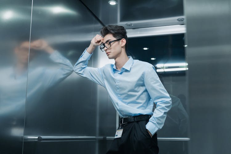 A Man In Blue Long Sleeves Wearing Eyeglasses Inside The Lift