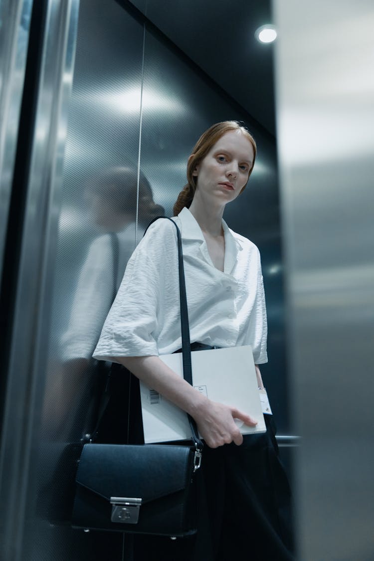 A Low Angle Shot Of A Woman In White Shirt While Holding A White Envelope Inside The Elevator