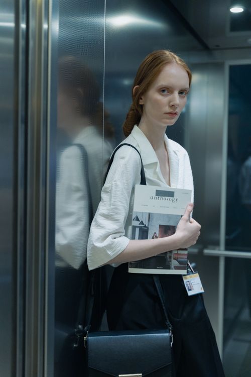 Free Caucasian woman in stylish attire holding a magazine in an elevator, showcasing modern fashion. Stock Photo