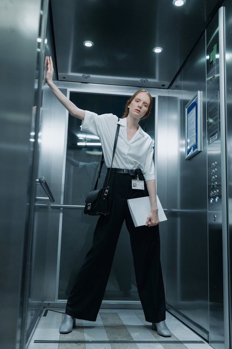 A Woman In White Button-Up Shirt Standing Inside The Elevator