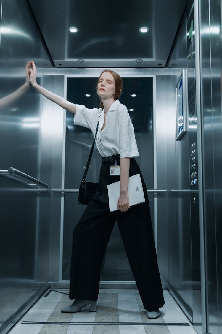 A Low Angle Shot Of A Woman In Black Pants And White Shirt Standing Inside The Lift