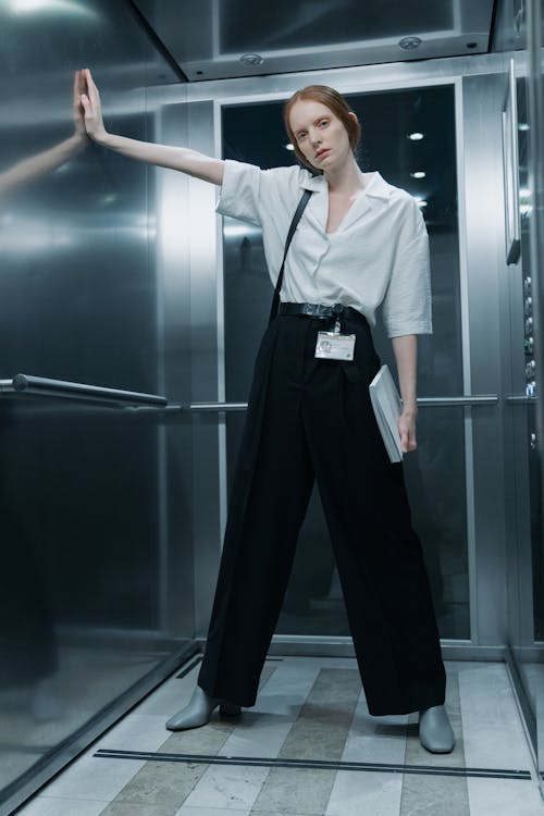Free A Woman in White Button-Up Shirt Standing inside the Elevator while Looking at Camera Stock Photo
