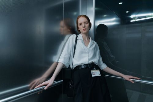 Free Woman in button down shirt standing in elevator, reflecting on glass walls. Stock Photo