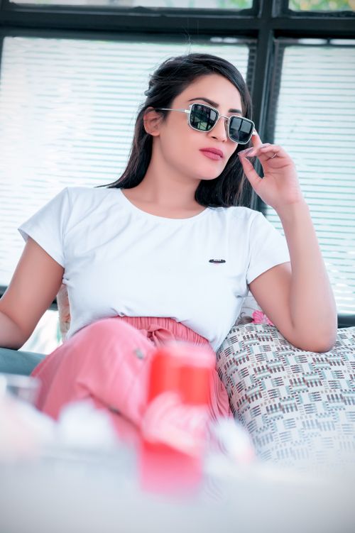 Free Elegant woman wearing sunglasses and pink attire, sitting comfortably indoors. Stock Photo