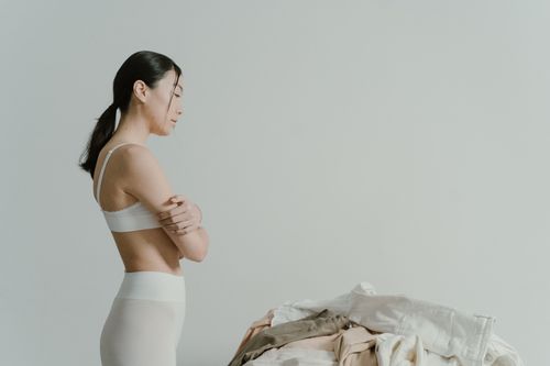 Free Asian woman in underwear standing with arms crossed near a pile of folded clothes. Stock Photo