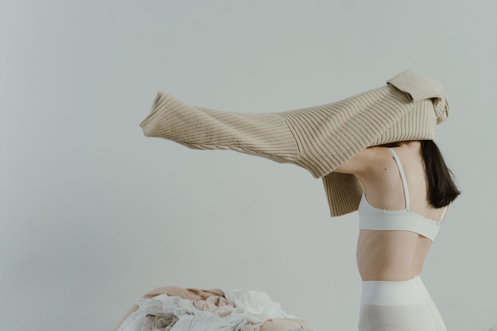 Woman putting on beige sweater minimalist style