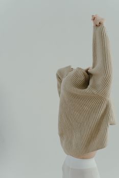 A close-up of a person stretching in a beige sweater, showcasing minimalist fashion style.