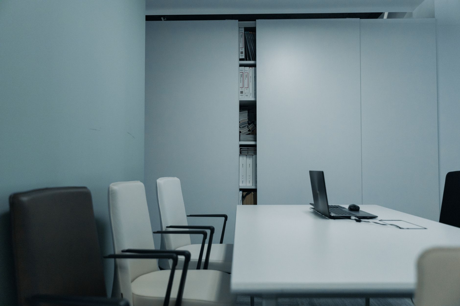 A sleek conference room with a white table and chairs, featuring a laptop on the table.
